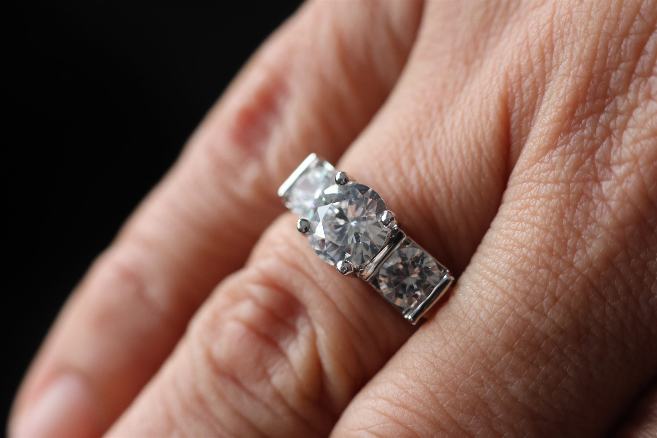 A three-stone diamond ring worn on a hand, shot close in low light.