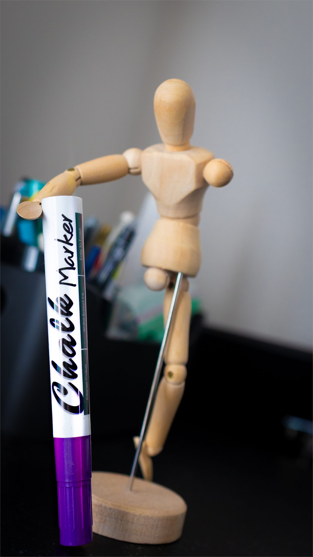 A purple liquid chalk marker leaning against a wooden artist's mannequin on a desk.