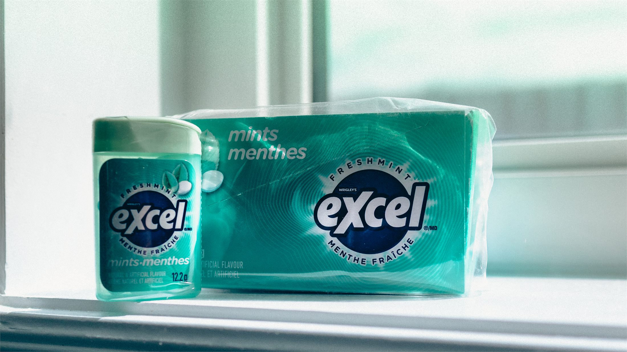 A tin and box of Excel Freshmint mints on a bright windowsill.
