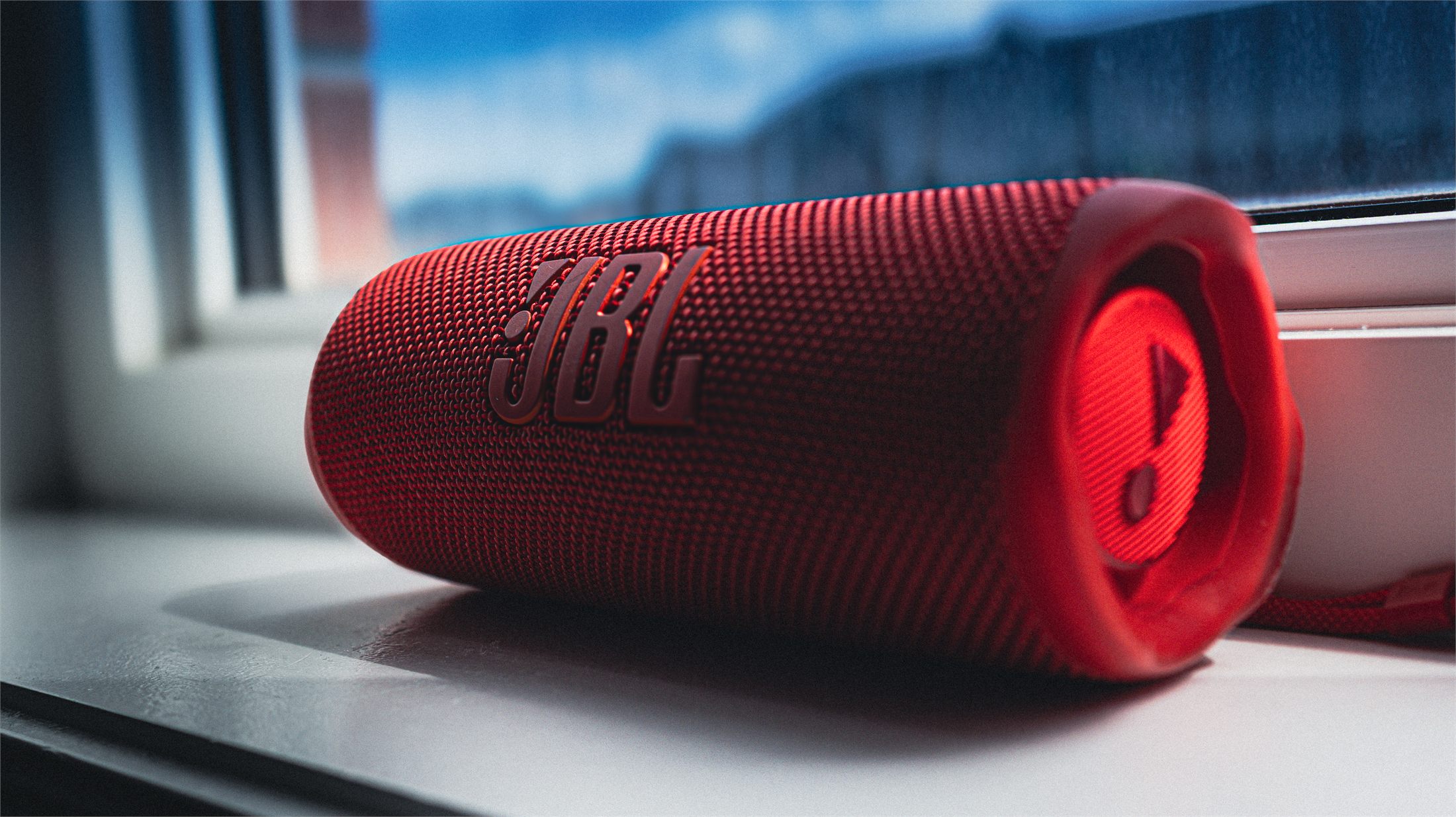 A red JBL portable speaker resting on a windowsill against a blue dusk sky.
