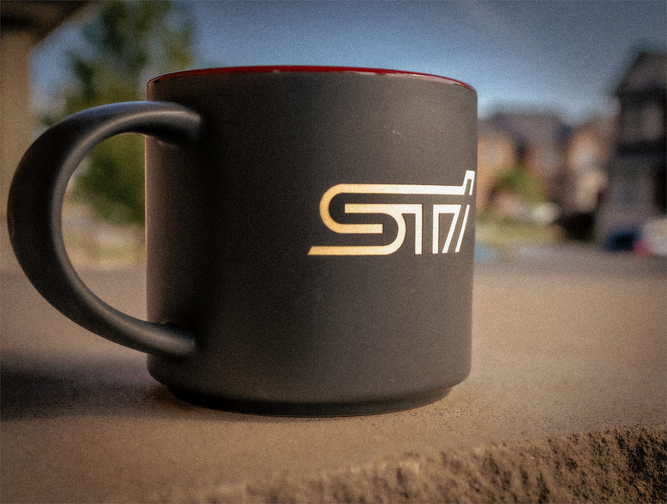 A matte black STI mug with a red interior, backlit at golden hour.