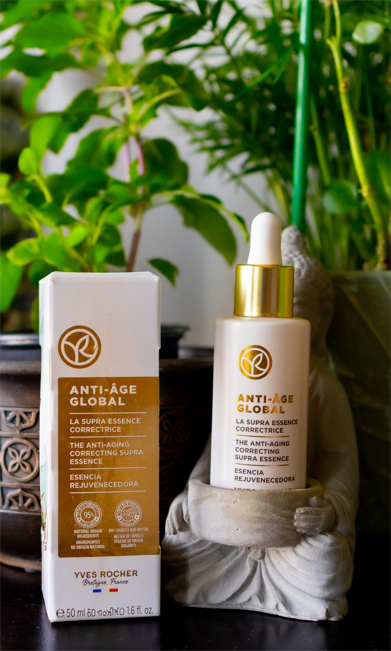 The Yves Rocher essence bottle and its Anti-Age Global box, the bottle held by a concrete monk figurine.